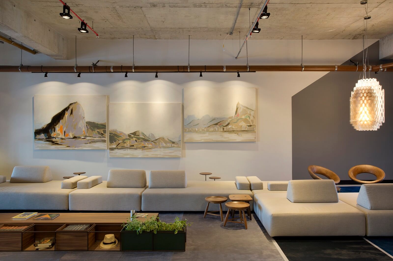 sala branca com gesso utilizando estilo industrial com sofás brancos, luminária e um quadro com uma paisagem de montanha dividida em 3 quadros que se complementam.