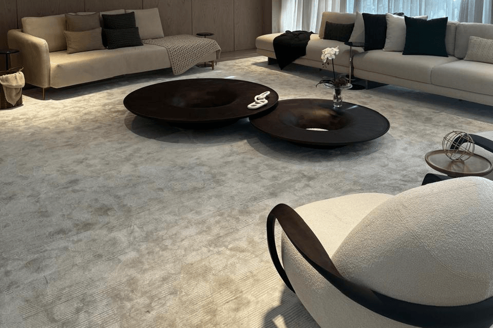 Novo luxo no mercado imobiliário: experiência e bem-estar 1 Ambiente de convivência amplo com dois sofás claros, mesas de centro redondas em madeira escura e cortinas com luz indireta