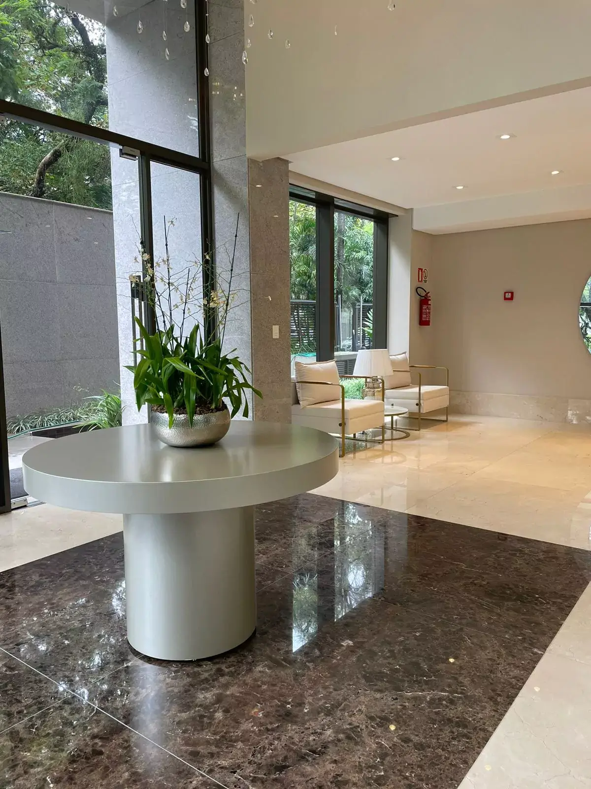 Mobiliário em empreendimentos: do imóvel ao estilo de vida 2 Hall de edifício residencial com mesa central redonda, orquídeas e poltronas brancas de estrutura dourada.