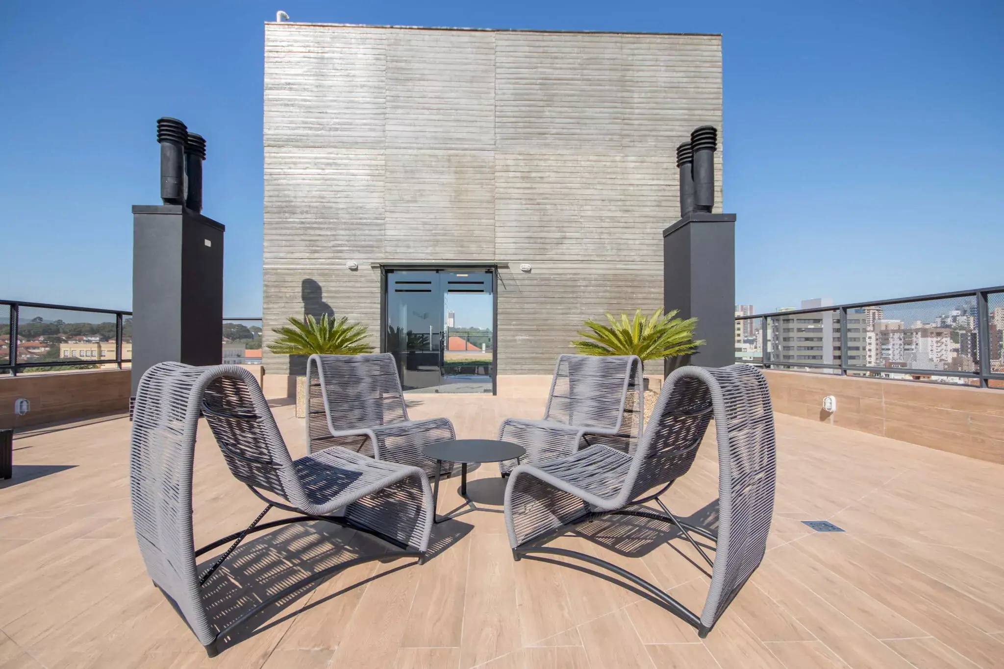 Mobiliário em empreendimentos: do imóvel ao estilo de vida 3 Rooftop de edifício com quatro poltronas em corda náutica cinza ao redor de mesa lateral redonda e vista da cidade