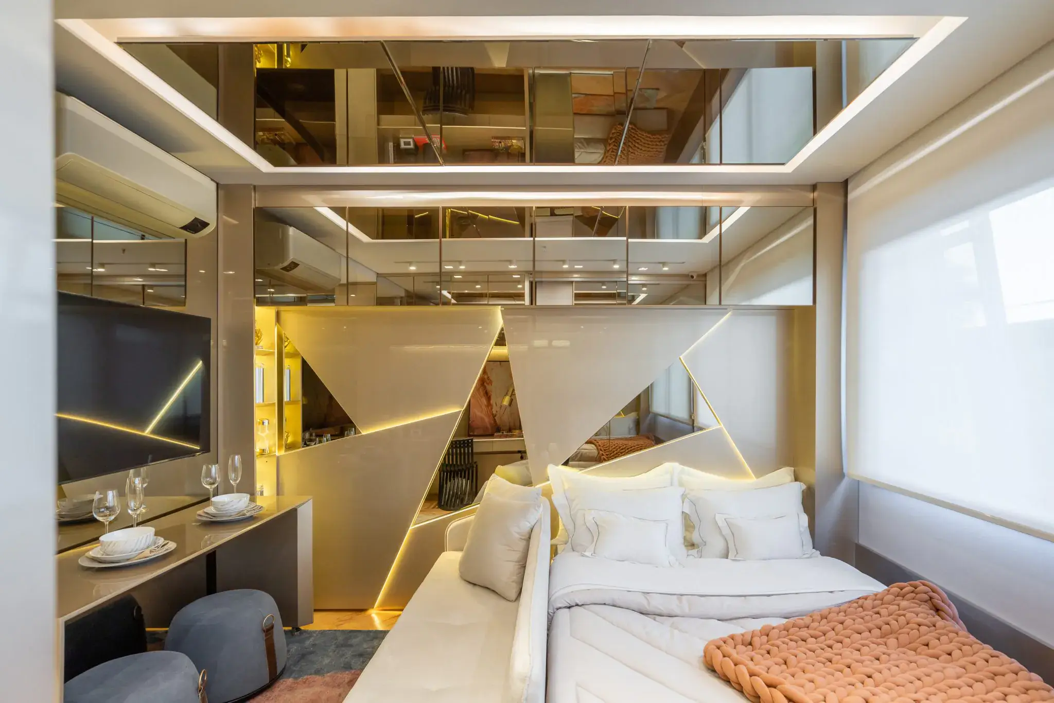 Mobiliário em empreendimentos: do imóvel ao estilo de vida 4 Studio decorado com cama, bancada que serve de mesa de refeições, pufes e painel geométrico com iluminação embutida