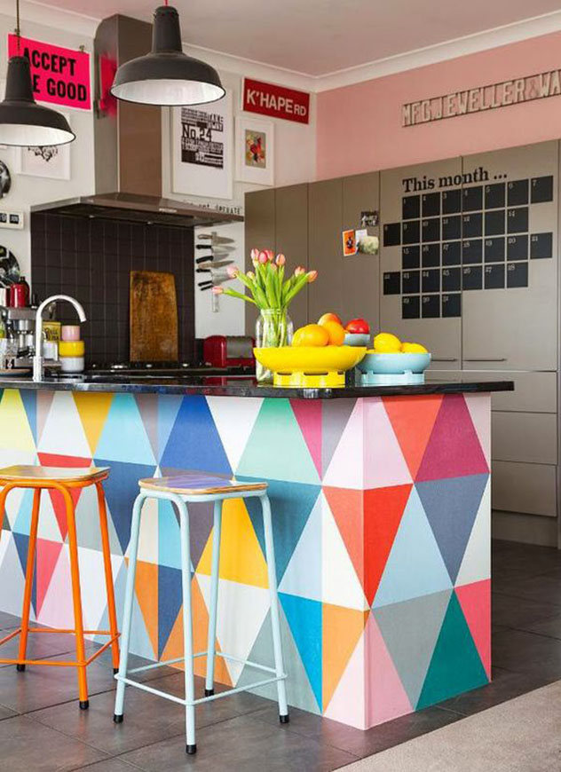 Nesta cozinha americana o balcão pintado com triângulos coloridos dá o tom alegre ao ambiente, que tem duas banquetas do mesmo modelo, porém em cores diferentes.