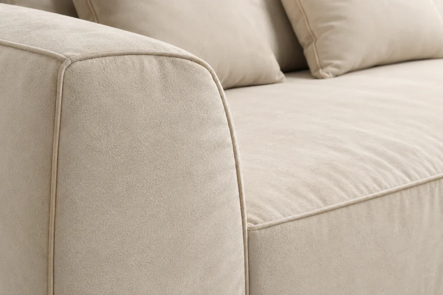 Detalhe do Sofá Brio em tecido com toque em suede no tom Areia, destacando a textura macia do revestimento, o braço arredondado e o acabamento com cordão vivo.