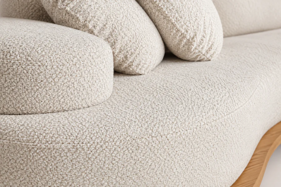 Detalhe do Sofá Curvo Orgânico Carvalho em tecido bouclé Off White, com textura encorpada, almofadas estofadas e base curva em acabamento laminado Freijó.