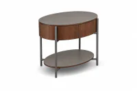 Mesa de Cabeceira Oval Olivar vista em perspectiva à direita, com design curvo, acabamento Nogueira, recouro Cinza com costuras aparentes e base aço carbono Grafite.
