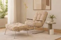 Poltrona de Balanço Raika em Bouclé Creme com estrutura metálica Champanhe Acetinado e puff combinando, ambientada em sala de estar contemporânea com luminária de piso dourada, mesa lateral redonda e decoração em tons neutros.