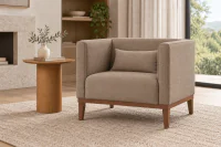 Poltrona Quadrada Trevi em tecido tramado Taupe, com braços altos, almofada de apoio lombar e base em madeira Nogueira, ambientada em sala de estar contemporânea ao lado de mesa lateral redonda de madeira.